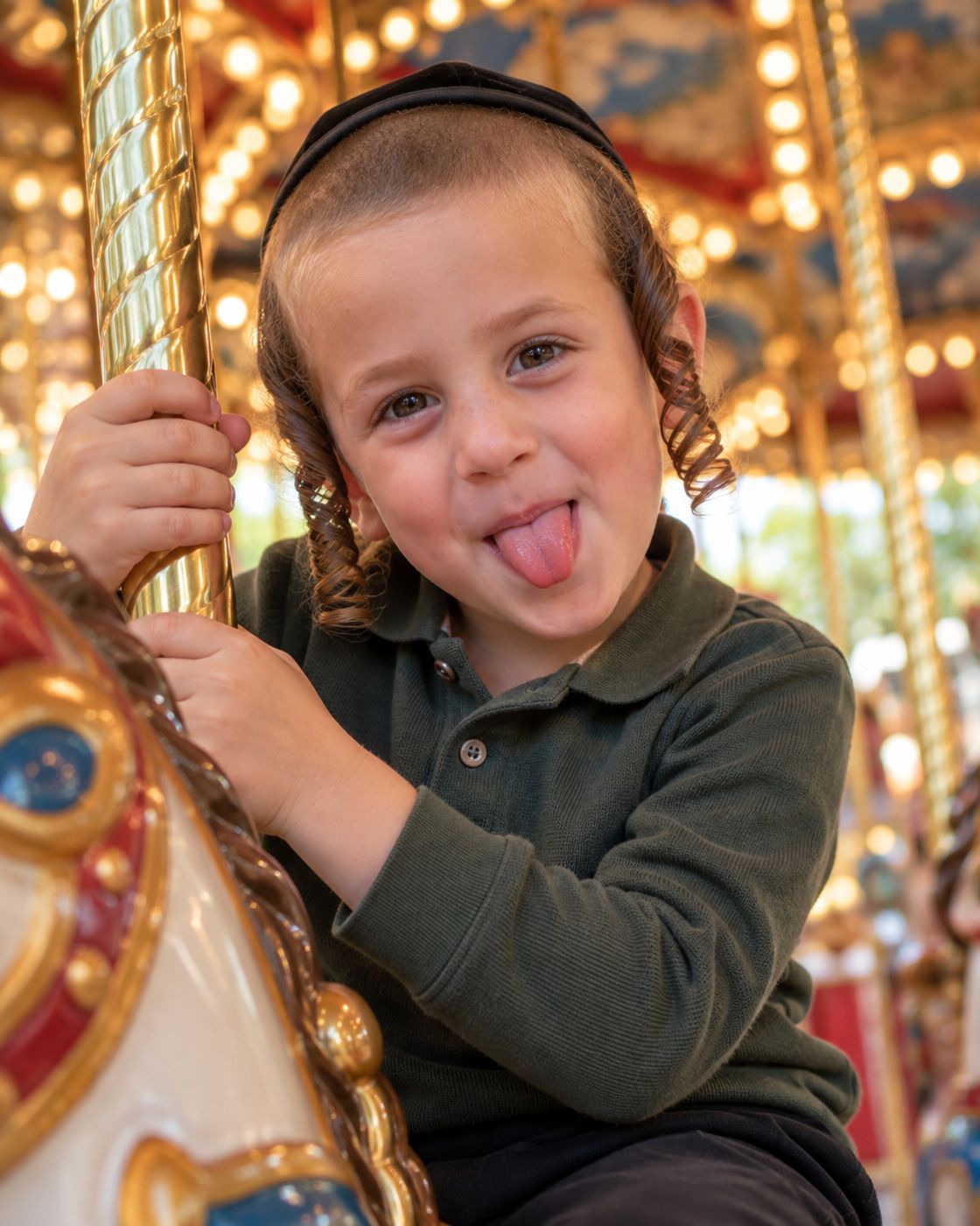 Boy with payos sticking out his tongue on a carousel horse